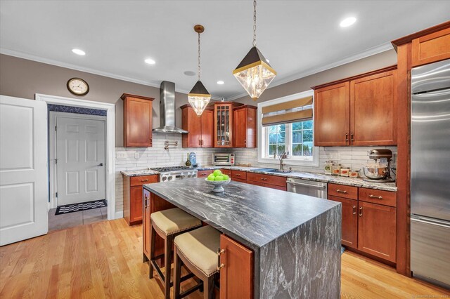 kitchen featuring a center island, wall chimney exhaust hood, stainless steel appliances, hanging light fixtures, and a breakfast bar