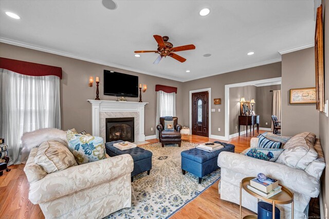 living room with ceiling fan, a high end fireplace, crown molding, and light hardwood / wood-style floors