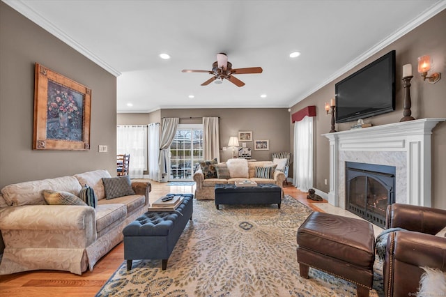 living room with ceiling fan, a high end fireplace, ornamental molding, and light hardwood / wood-style flooring