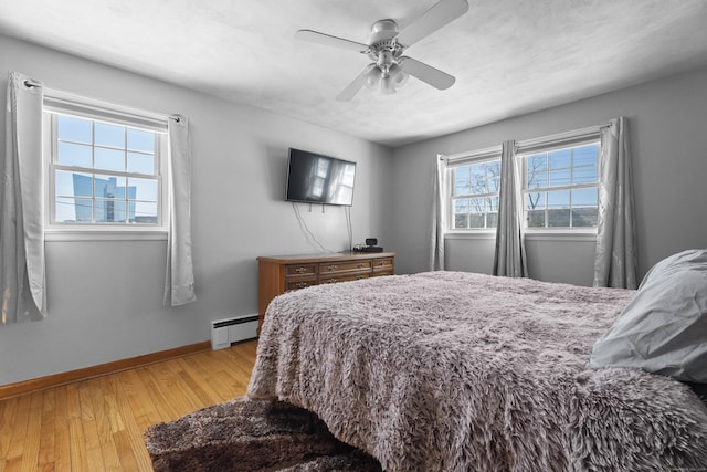 bedroom with multiple windows, light hardwood / wood-style flooring, ceiling fan, and baseboard heating