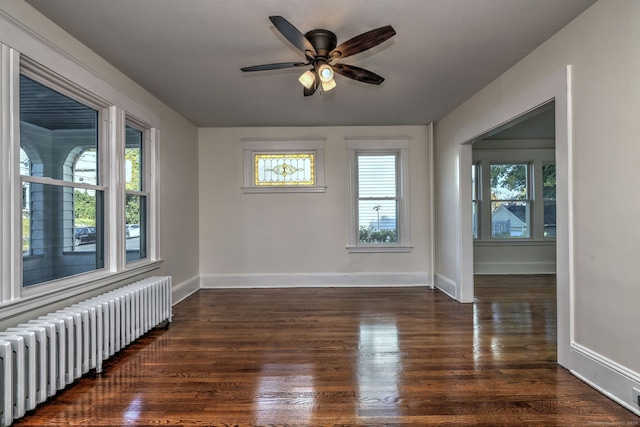 empty room with radiator heating unit, ceiling fan, a healthy amount of sunlight, and dark wood-type flooring