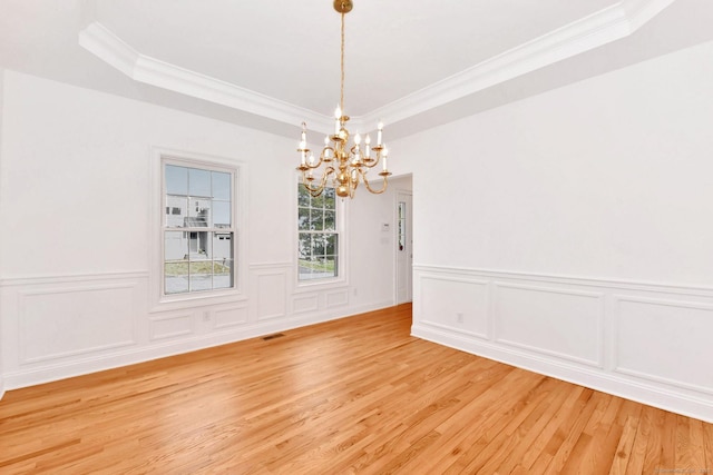 empty room with a notable chandelier, a tray ceiling, wood-type flooring, and ornamental molding