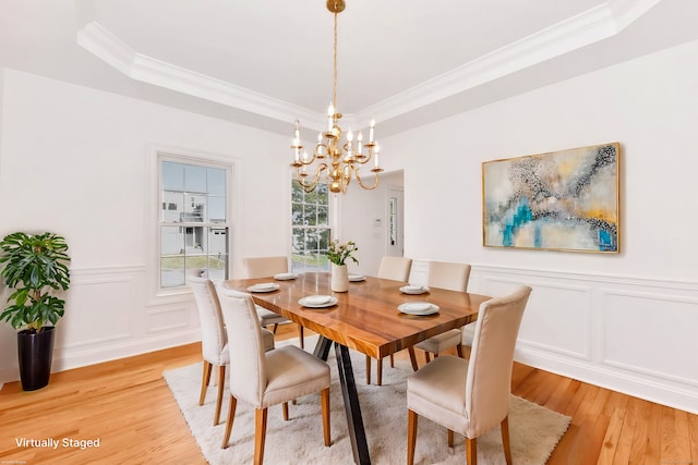 dining space with a raised ceiling, crown molding, an inviting chandelier, and light hardwood / wood-style flooring