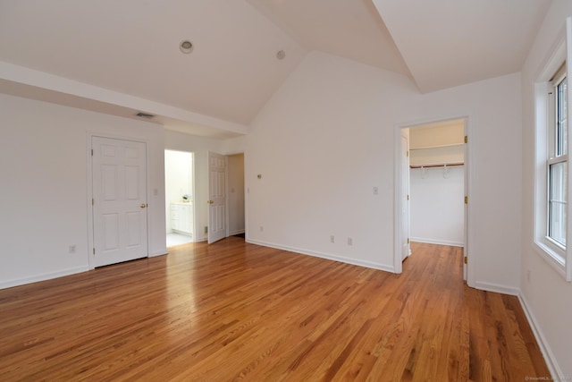 unfurnished bedroom with a walk in closet, high vaulted ceiling, and light wood-type flooring