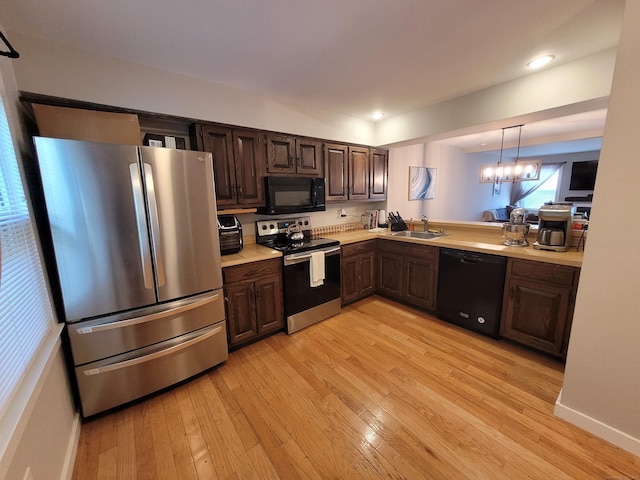 kitchen with hanging light fixtures, black appliances, an inviting chandelier, light wood-type flooring, and dark brown cabinetry