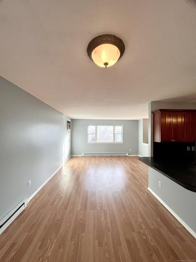 unfurnished living room featuring baseboard heating, light hardwood / wood-style floors, and a wall mounted air conditioner