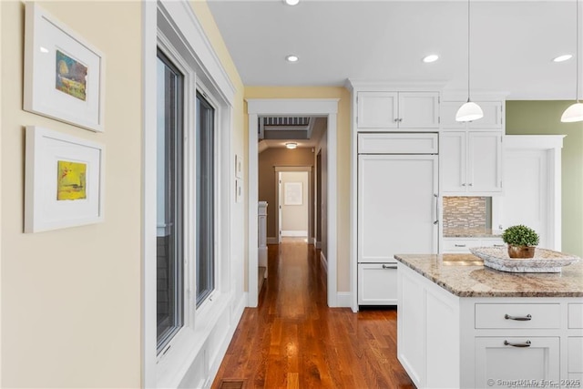 kitchen featuring backsplash, paneled built in fridge, light stone countertops, pendant lighting, and white cabinets