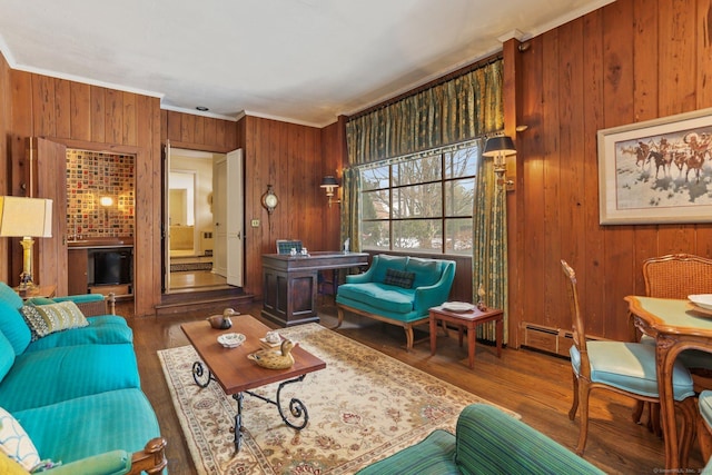 living room with baseboard heating, wood-type flooring, crown molding, and wood walls