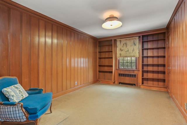 sitting room featuring built in features, radiator, light carpet, and wood walls