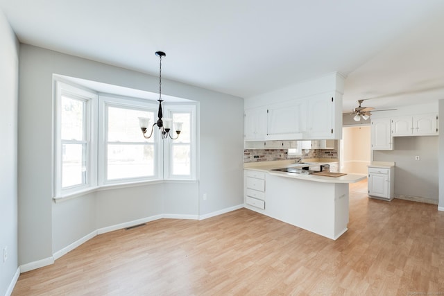 kitchen with decorative light fixtures, white cabinets, decorative backsplash, kitchen peninsula, and light hardwood / wood-style flooring