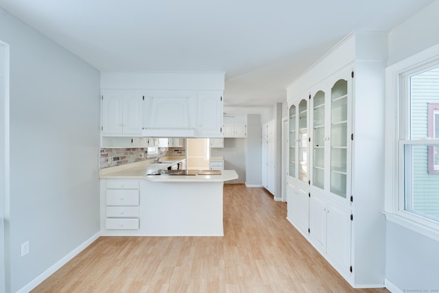 kitchen featuring sink, light hardwood / wood-style flooring, white cabinetry, backsplash, and kitchen peninsula