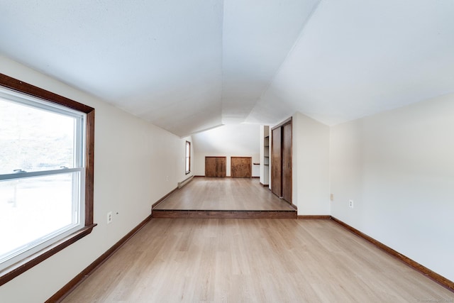 bonus room with built in shelves, lofted ceiling, and light hardwood / wood-style flooring