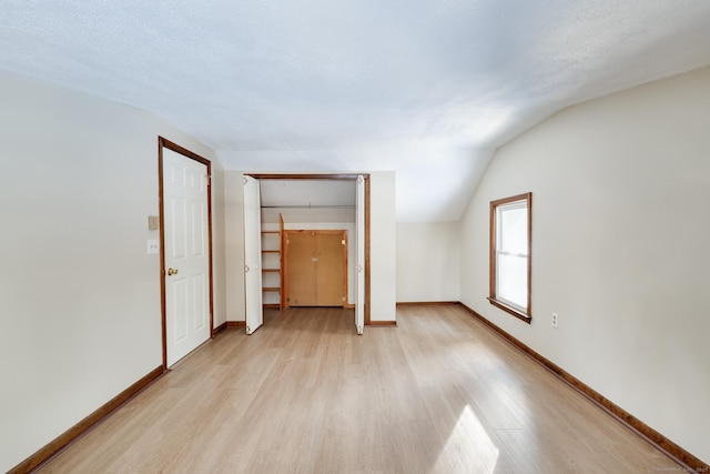 empty room with vaulted ceiling, light hardwood / wood-style floors, and a textured ceiling