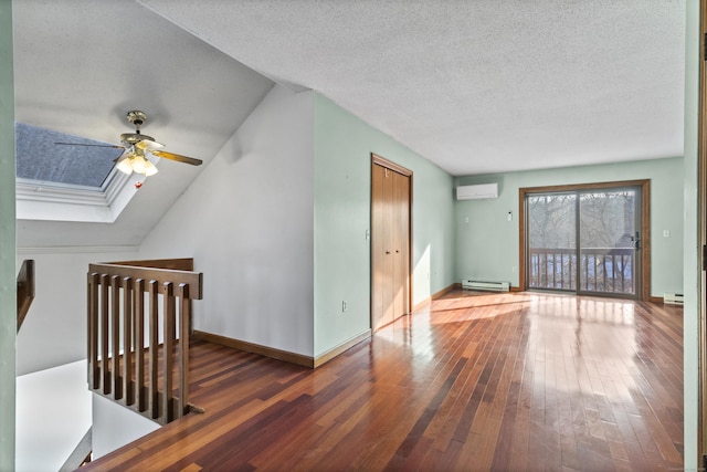 interior space featuring a wall mounted air conditioner, a baseboard radiator, hardwood / wood-style flooring, ceiling fan, and vaulted ceiling with skylight