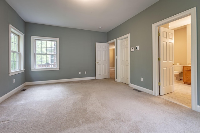 unfurnished bedroom featuring ensuite bathroom, light carpet, baseboards, and visible vents