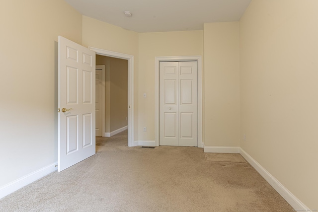 unfurnished bedroom featuring light colored carpet, a closet, baseboards, and visible vents