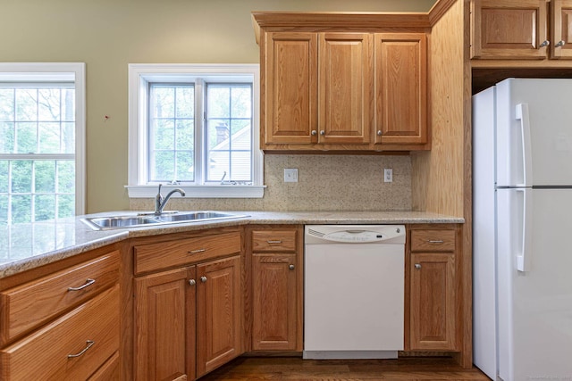 kitchen with a sink, brown cabinetry, white appliances, wood finished floors, and light countertops