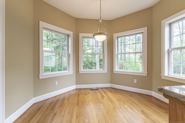 unfurnished dining area featuring light wood-type flooring, visible vents, and baseboards