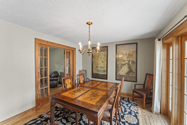 dining area featuring light wood-type flooring, an inviting chandelier, french doors, and a textured ceiling