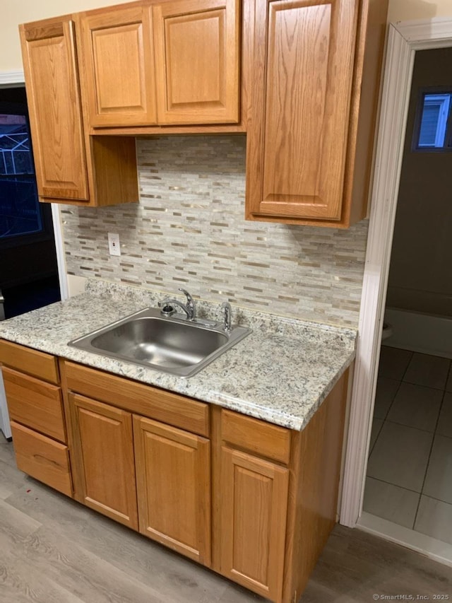 kitchen with sink, light hardwood / wood-style floors, decorative backsplash, and light stone countertops