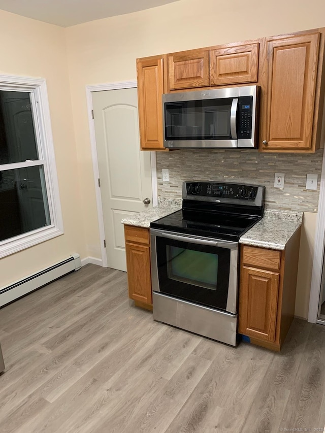 kitchen with light stone countertops, a baseboard radiator, appliances with stainless steel finishes, light hardwood / wood-style floors, and decorative backsplash