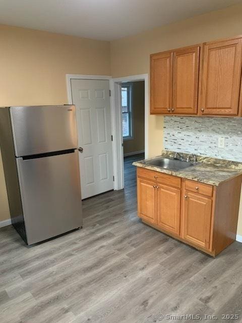 kitchen featuring decorative backsplash, sink, stainless steel fridge, and light hardwood / wood-style flooring