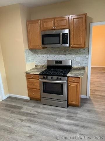 kitchen with light wood-type flooring, backsplash, and appliances with stainless steel finishes