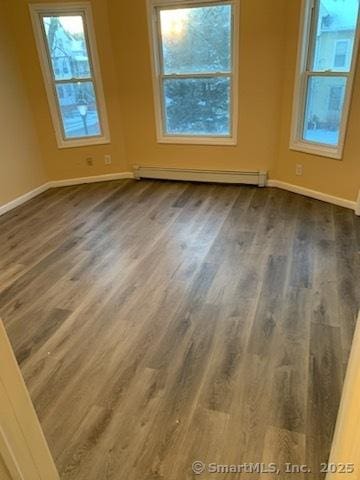 unfurnished room featuring baseboard heating and dark hardwood / wood-style flooring