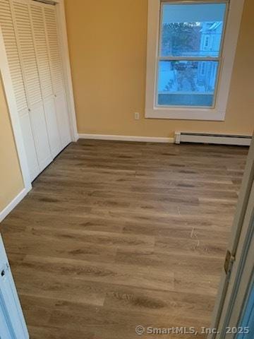 unfurnished bedroom with a closet, a baseboard heating unit, and dark hardwood / wood-style flooring