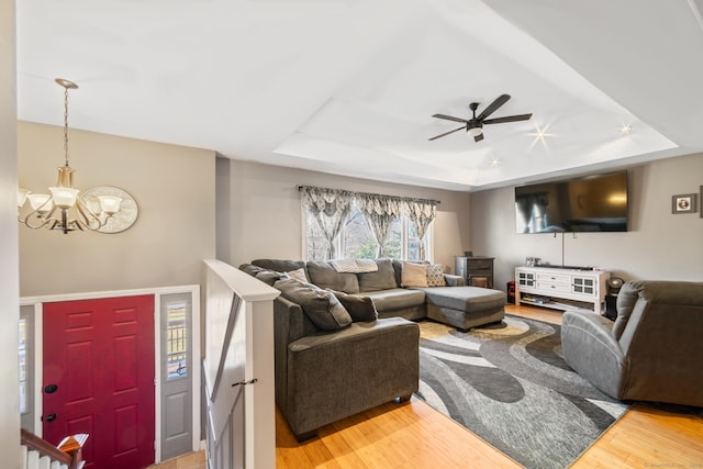 living room with wood-type flooring, ceiling fan with notable chandelier, and a raised ceiling