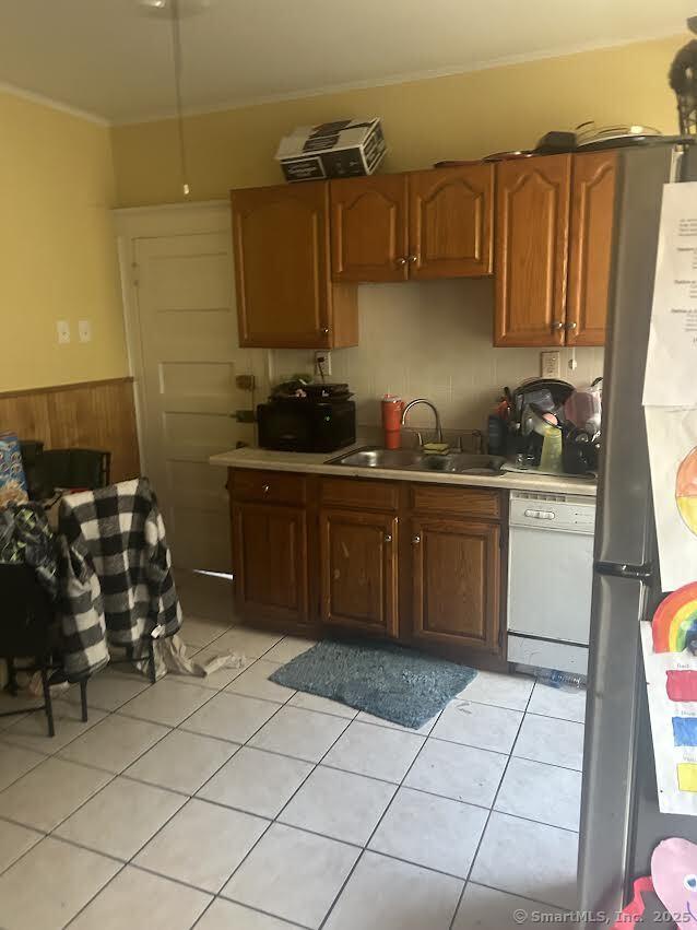 kitchen featuring white dishwasher, stainless steel fridge, wooden walls, sink, and light tile patterned flooring