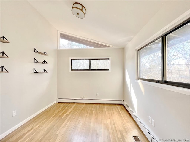 spare room featuring plenty of natural light, a baseboard radiator, light wood-type flooring, and vaulted ceiling