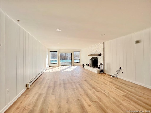 unfurnished living room with baseboard heating, a brick fireplace, wood walls, and light hardwood / wood-style flooring