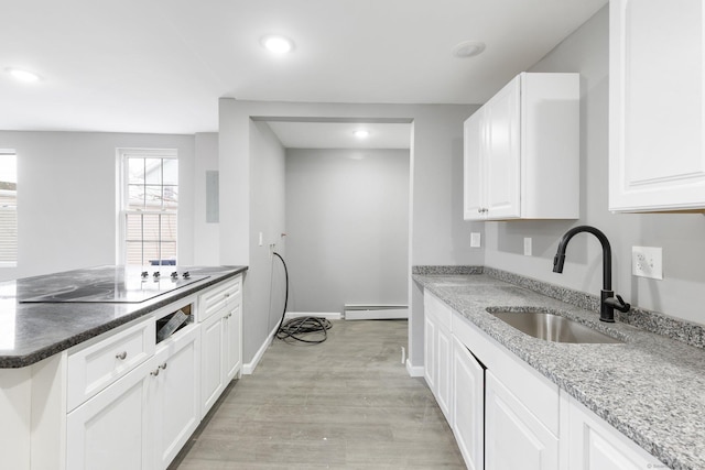 kitchen featuring dark stone countertops, black electric cooktop, sink, white cabinetry, and a baseboard radiator