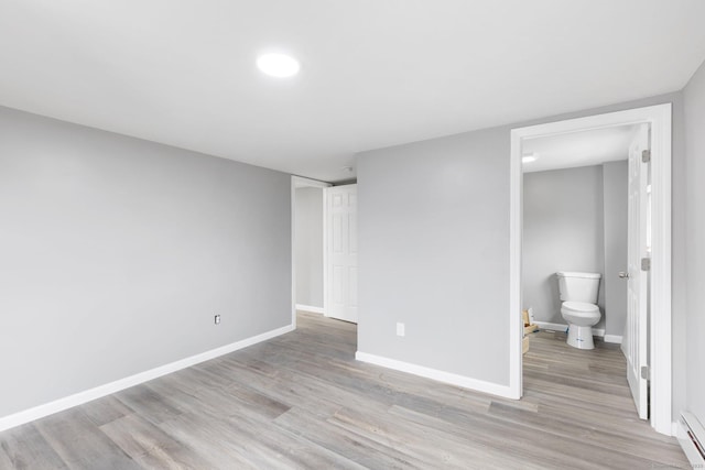 unfurnished bedroom with a baseboard radiator, connected bathroom, and light hardwood / wood-style flooring