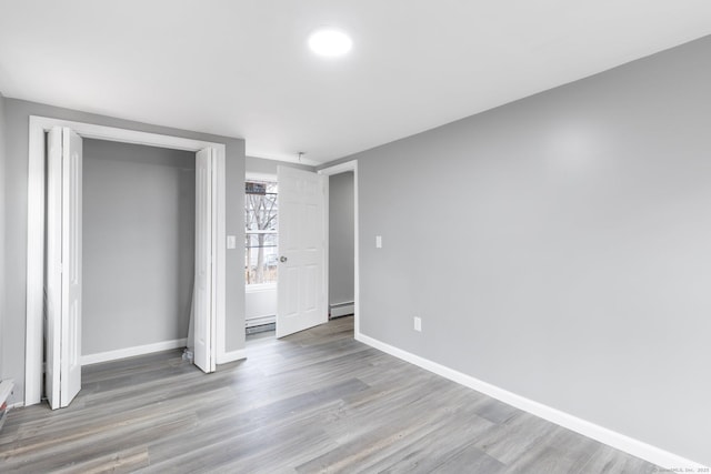 unfurnished bedroom with a closet, a baseboard heating unit, and light hardwood / wood-style floors