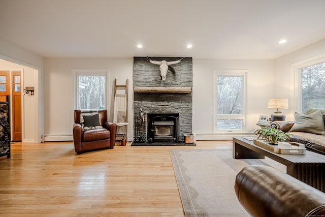 living room with baseboard heating, a wood stove, and light hardwood / wood-style floors