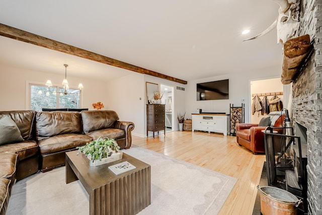 living room with a fireplace, beam ceiling, light hardwood / wood-style floors, and an inviting chandelier