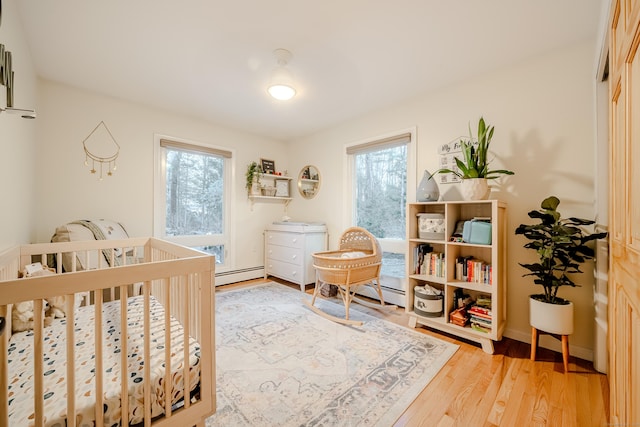 bedroom with a nursery area, hardwood / wood-style flooring, multiple windows, and a baseboard radiator