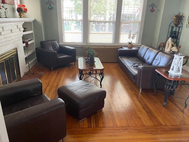 living room featuring a brick fireplace, built in shelves, and hardwood / wood-style floors