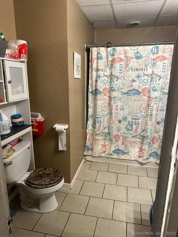 bathroom with a paneled ceiling, tile patterned floors, a shower with shower curtain, and toilet