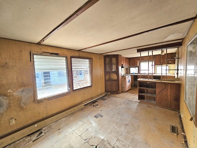 kitchen featuring beam ceiling, wooden walls, white gas stove, and plenty of natural light