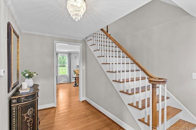 staircase with a notable chandelier, ornamental molding, and hardwood / wood-style floors