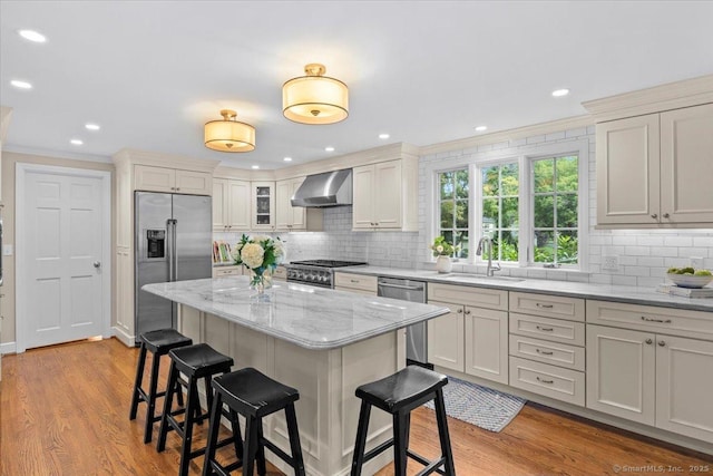 kitchen featuring wall chimney range hood, sink, light hardwood / wood-style flooring, stainless steel appliances, and light stone counters