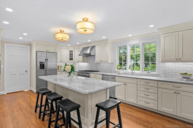 kitchen with appliances with stainless steel finishes, decorative backsplash, light wood-type flooring, wall chimney range hood, and sink