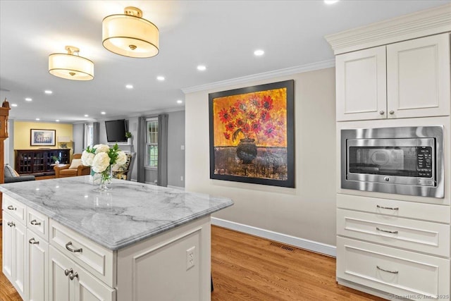 kitchen featuring stainless steel microwave, crown molding, white cabinetry, light wood-type flooring, and light stone counters