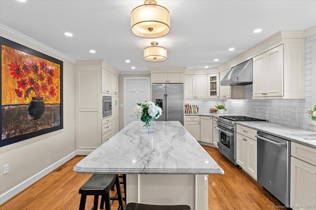 kitchen featuring a kitchen island, white cabinetry, premium appliances, wall chimney exhaust hood, and light stone counters