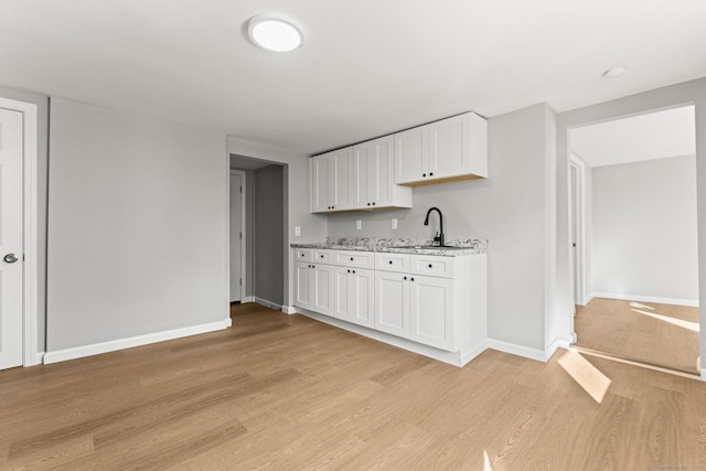 kitchen with white cabinets, sink, light stone counters, and light hardwood / wood-style flooring