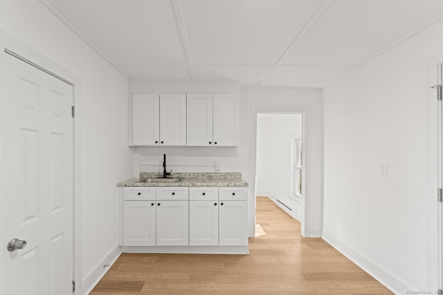 kitchen with light wood-type flooring, light stone countertops, white cabinetry, and sink