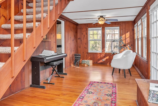 living area featuring ceiling fan, wood walls, and light hardwood / wood-style floors